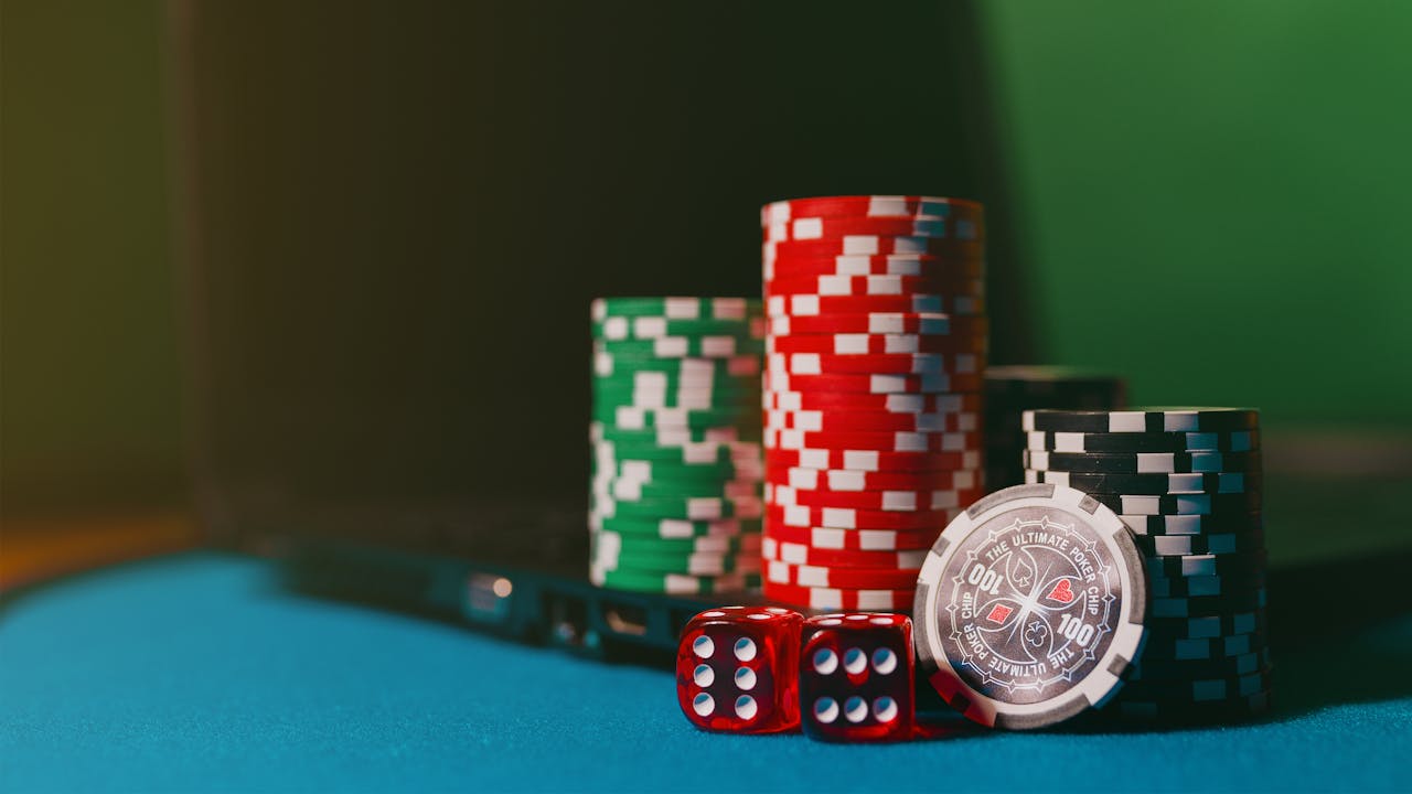 hero-img-02 Close-up of casino chips and dice on a felt table, next to a laptop for online gambling.