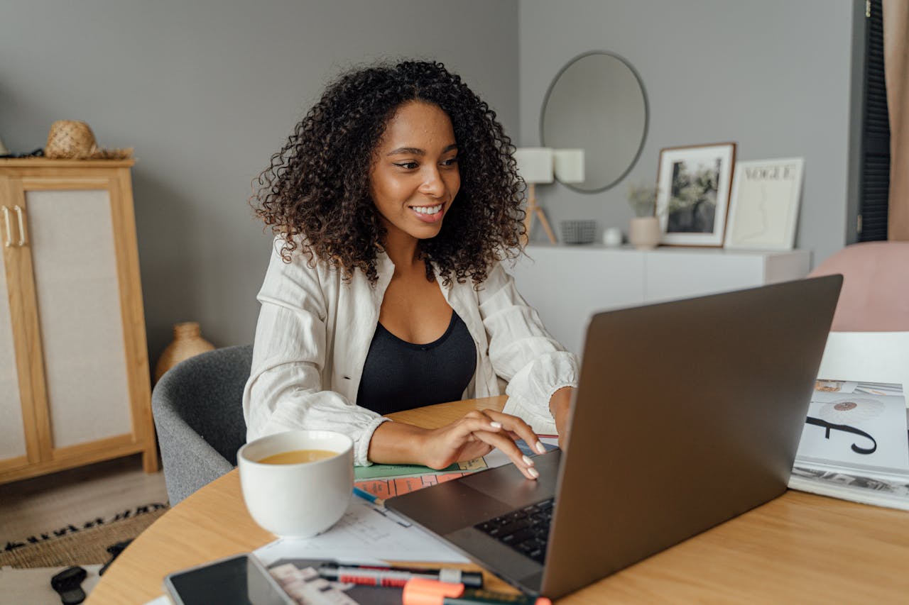 about-01 A woman sits at a round table, working on a laptop with a coffee cup nearby in a cozy home office setting.